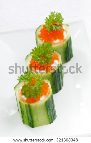 cucumber tartlets with cream cheese and red caviar, vertical top view, selective focus