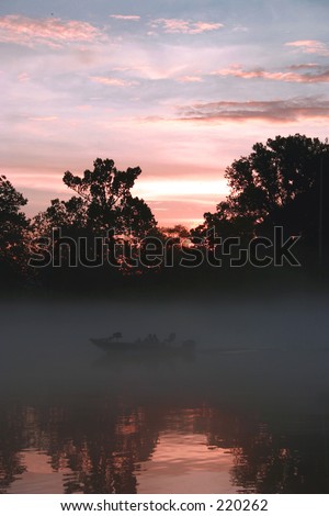 A fishing boat on this lake shrouded with fog at sunset
