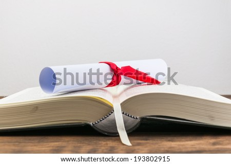 A parchment diploma scroll, rolled up with red ribbon on book on wood background