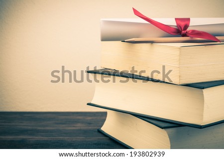 A parchment diploma scroll, rolled up with red ribbon on stack of book on wood background with vintage filter