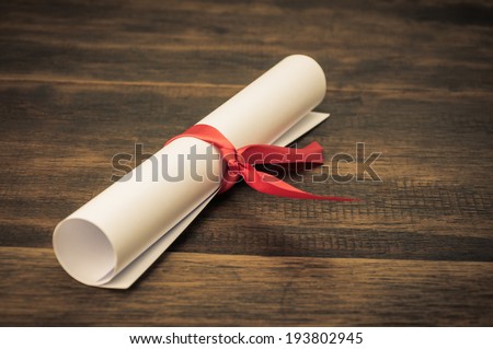 A parchment diploma scroll, rolled up with red ribbon on wooden backgroung