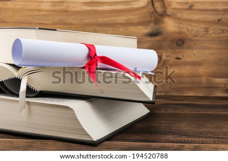 A parchment diploma scroll, rolled up with red ribbon on stack of book on wood background