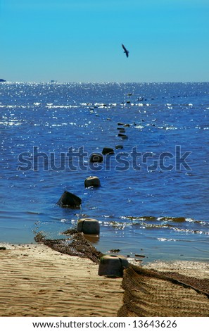 Sandy coast of the dark blue sea under the blue sky. Fishing network with floats on sand and in the sea