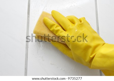 Hand in yellow glove with sponge, washing bathroom\'s wall