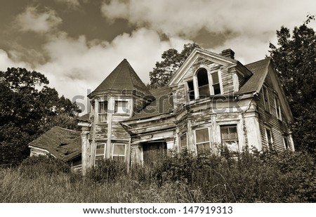Old abandoned haunted house overgrown with weeds against a dark sepia sky
