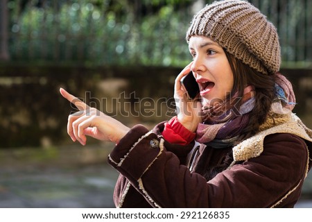 Surprised woman pointing out while talking on a cell phone. Travel, technology and communication.