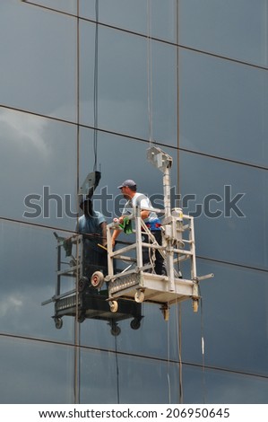 ATHENS, GREECE - JULY 24, 2014: Man cleaning the windows of high rise building glass facade. Working at height dangerous occupation.