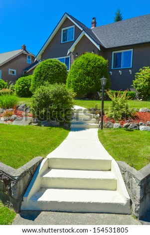 Front pathway with steps leading to a house. Front yard of Canadian house with landscaping. Family house on blue sky background in Vancouver, Canada.