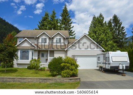 North American family house on country side. Single house with landscaping on the front and blue sky background. RV parked on concrete driveway beside the house