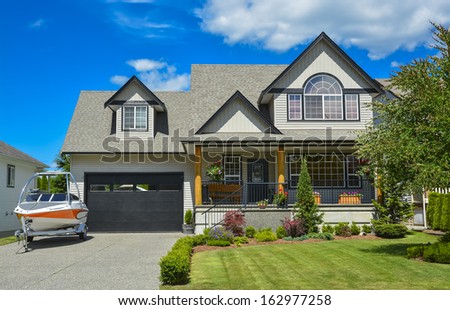 Suburban house with landscaping in front and blue sky background. Light powerboat parked on concrete driveway in front of the house.