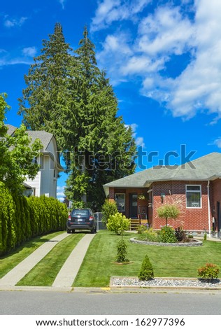 Fragment of a house with traced driveway and parked car on it. Fragment of a house with trees and blue sky on background.
