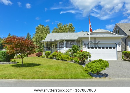 Family house on a sunny day with Canadian flag on the front yard and blue sky background. British Columbia, Canada.