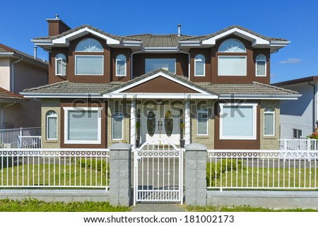 Suburban Vancouver house with metal fence and gate in front and blue sky background.