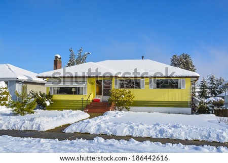 Family houses at winter season. Residential house in snow on a sunny day. Yellow house in snow on blue sky background.