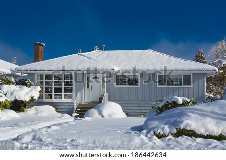 Family house at winter season. Residential house in snow on a sunny day. Grey house in snow on blue sky background.