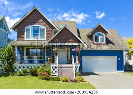Blue residential house with concrete driveway in front and blue sky background.