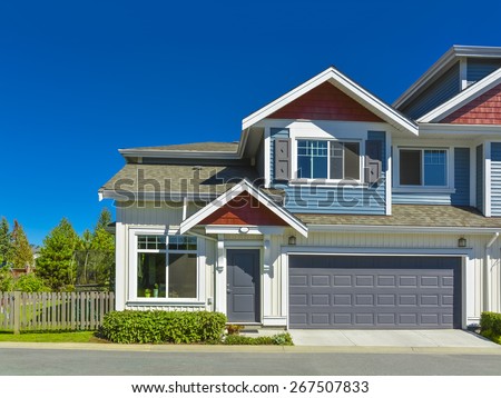 New residential townhouse with entrance and garage doors in front on sunny day, British Columbia, Canada. Garage with concrete driveway and asphalt road in front.