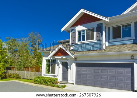 New residential townhouse on sunny day with wide garage door and concrete pathway in front. British Columbia, Canada.