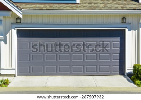 Wide garage door of residential townhouse on sunny day, British Columbia, Canada. Double garage of family townhouse with concrete driveway.