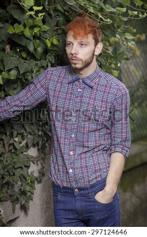 Fashionable red haired model posing outdoors, looking to the left. Wearing shirt, and jeans.