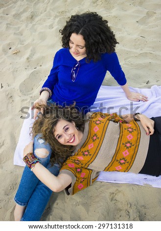 Two friends relaxing on a beach, sitting near each other on a towel.