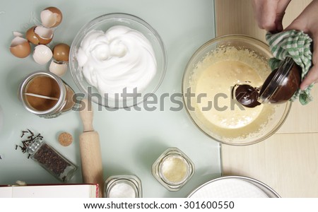 Hand mixing chocolate with eggs, on kitchen table full of other ingredients, shot from above. Shot from above.