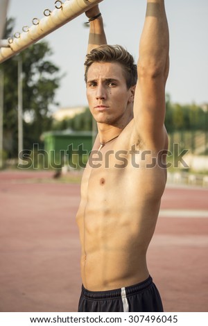 Beautiful athlete relaxing while doing pull ups. Muscular upper body, with strong abs.