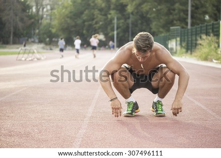 Tired sprinter at start position kneeling. Other runners out of focus.