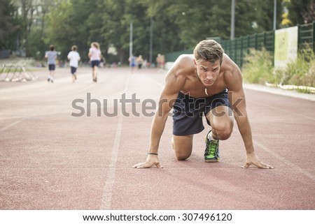 Sprinter at start position, kneeling, muscular body.