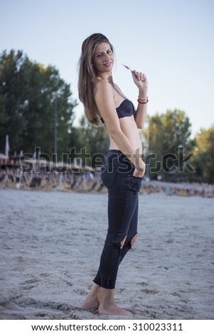 Sexy girl on a beach, from from side. Wearing jeans, and bikini.
