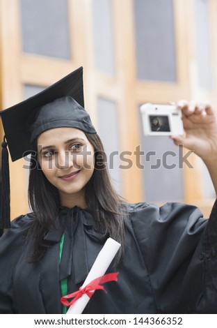Woman in graduation gown taking a picture of herself with a digital camera