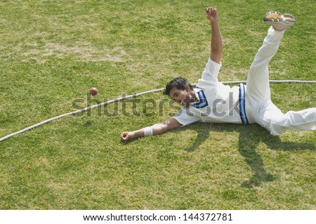 Cricket fielder diving to stop a ball near boundary line