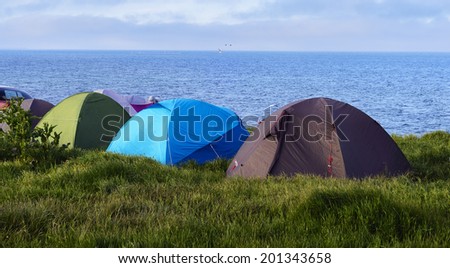 Camping with tent on green grass at seaside with blue sea on background