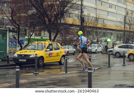 BUCHAREST, ROMANIA - MARCH 03, 2015 : Young man in athlete clothing, running in the rain on the streets of Bucharest