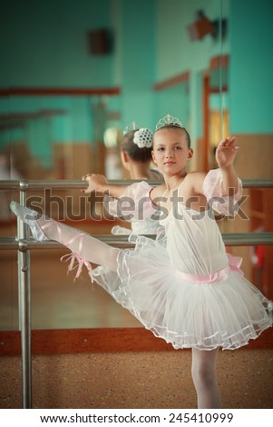 A little adorable young ballerina in a white tutu near the mirror