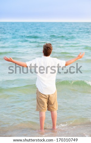 boy raising hands in waves on the beach