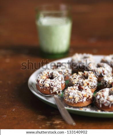 Donuts with coconut and chopped hazelnuts on plate and a glass of milk