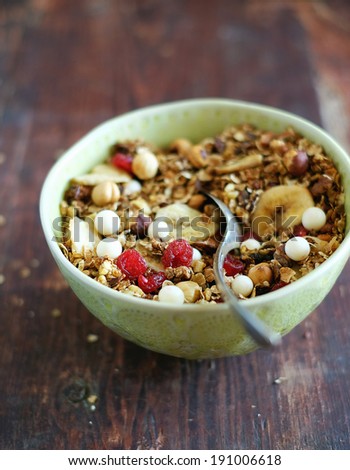 Healthy homemade granola or muesli with toasted oats, dried cherry, cranberry, figs, raisin, hazelnuts, cashew, walnuts, yogurt and white chocolate chips and honey in a bowl for breakfast or snack