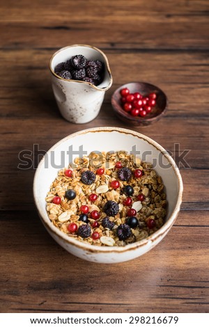 Granola or muesli with oats, fresh berries and nuts in a bowl with a cup of fresh blackberry and a little plate of red currant, selective focus