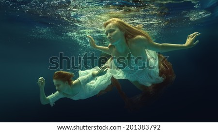 Woman and girl in beautiful dresses swim underwater.