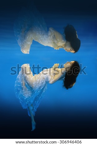 The girl in a beautiful dress underwater with reflection.