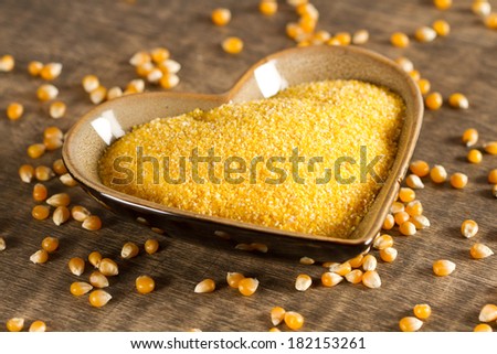 Corn grits in heart shape bowl and corn seeds on old wooden background