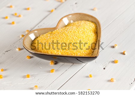 Corn grits in heart shape bowl and corn seeds on white wooden background