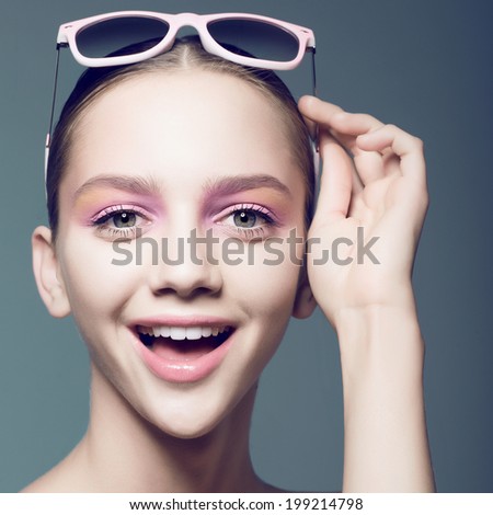 Portrait of a beautiful young girl in studio with sunglasses on a blue background, smiley face, close up
