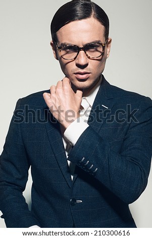 Handsome young man in a suit and fashionable glasses, posing in studio