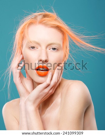 Portrait of beautiful young girl with orange hair on a blue background, surprise