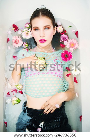 Portrait of beautiful young brunette girl with bright makeup lying in the bath with flowers