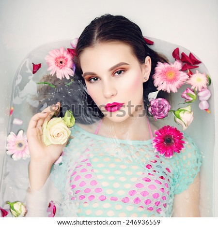 Portrait of beautiful brunette girl with bright makeup lying in the bath with flowers, the concept of health and beauty