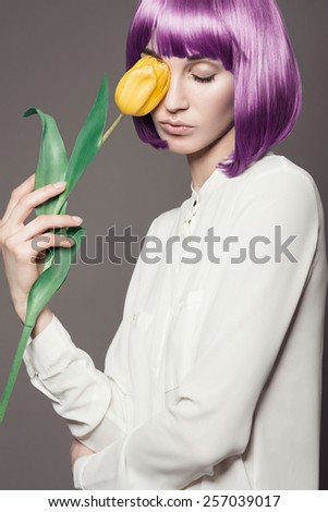 Portrait of beautiful girl with purple hair and yellow tulips in the studio on a gray background, the concept of health and beauty