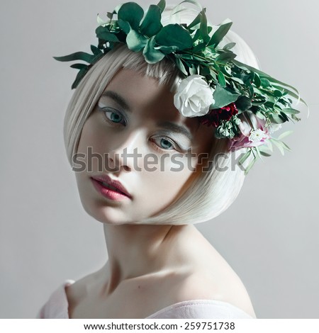 Portrait of a beautiful young blond woman with short hair and a wreath of flowers in the studio, close up